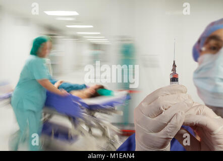 Ein Arzt mit Spritze und Handschuhe über Motion verschwommenen Hintergrund der Krankenschwester, die in Eile Wurf nach unten schieben eine sterile Licht Krankenhaus Flur. Stockfoto