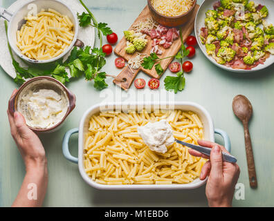 Kochen Vorbereitung der Amerikanischen Stil herzhaften Teigwaren Teigwaren in kitschig-Sauce. Weibliche hand pasta Auflauf mit Tomaten, Schinken und Käse, oben vie Stockfoto