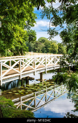 Einen hölzernen Brücke über Wasser von Woodland auf Felder, bei Stowe Landscape Gardens fotografiert, von Bäumen im Blatt gerahmt Stockfoto