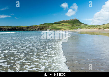 Eine sanfte Welle rollt über die Sande der Whitesands Bay, in der Nähe von St Davids, Wales, unter einem blauen Himmel mit flauschigen weissen Wolken über dem zerklüfteten Hügel Carn Llidi Stockfoto