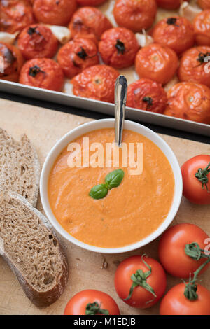 Hausgemachte Tomaten und Basilikum Suppe mit Schwarzbrot Neben gerösteten Tomaten und Knoblauch in einem Backblech auf einer Schiefertafel Hintergrund. Stockfoto