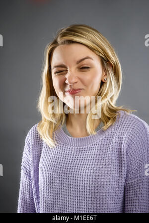 Junge Easten - europäische Frau mit langen blonden Haaren macht lustiges Gesicht in die Kamera auf grauem Hintergrund Stockfoto