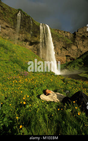 Island, der Wasserfall Seljalandsfoss, Frau entspannen im Gras. Stockfoto