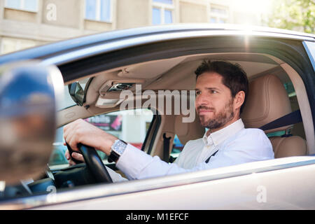 Lächelnden jungen Mann mit seinem Auto fährt während der morgendlichen Fahrt zum Arbeitsplatz Stockfoto