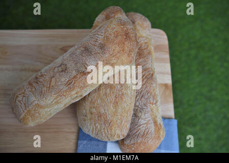 Rustikales essen Bild von hausgemachten artisan Ciabatta weißes Brot Brote auf Holzbrett mit grünem Gras Hintergrund für einen Sommer Picknick Einstellung Stockfoto