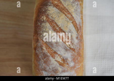 Rustikales essen Bild eines köstlichen hausgemachten frisch gebackenen Laib white Artisan Brot auf einem Holzbrett mit cremefarbenen Tischdecke Hintergrund Stockfoto