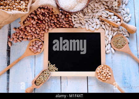 Verschiedene Arten von Bohnen um schwarz gerahmten Platz auf Blau Holztisch. Von oben. Stockfoto