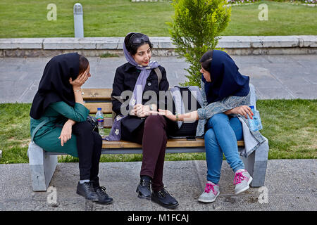 Isfahan, Iran - 24. April 2017: Drei hübsche iranische Frauen in hijabs sitzen auf einer Bank im Park und etwas besprechen. Stockfoto