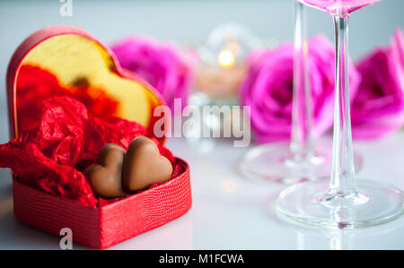 Red heart-shaped Box mit Schokolade Herzen, rose Blumen, zwei Gläser Champagner und eine Kerze. Stockfoto