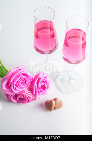 Schokolade Herzen, rosa Blüten und zwei Gläser Champagner Rosé. weißen Hintergrund. Selektive konzentrieren. Stockfoto