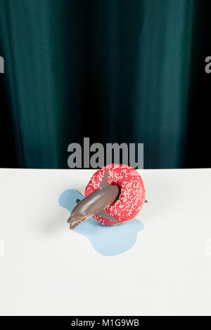 Ein Delphin aus Kunststoff Spielzeug in einem Donut symbolisiert eine Boje auf der Pfütze Form geschnitten aus blauen Papier auf weißem Hintergrund und eine pulsierende grüne Vorhang. Minderen Stockfoto