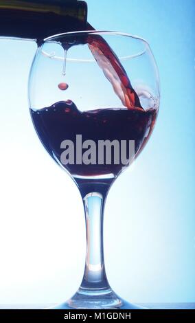 Rotwein gegossen in ein transparentes Glas Becher. Das Foto auf dem blauen Hintergrund. Stockfoto