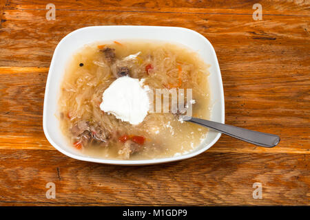 Russische Kohlsuppe mit Schmorkohl und Sauerrahm in Keramik Platte auf hölzernen Tisch Stockfoto