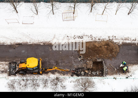 Oben Ansicht der Arbeitnehmer und der Traktor graben Straße Kanalrohre im Winter in Moskau Stadt zu ändern. Stockfoto