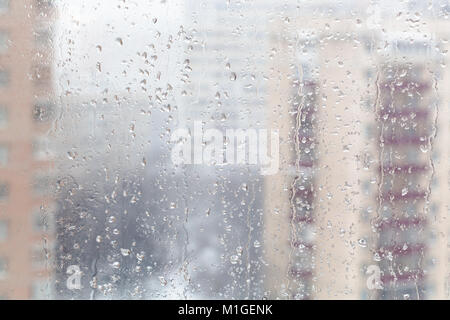 Im städtischen Hintergrund - Tropfen schmelzenden Schnee auf Fensterglas (Fokus auf Wasser rieselt auf Fensterglas) im Winter Stockfoto