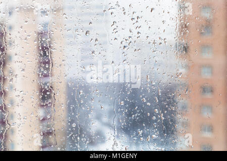 Im städtischen Hintergrund - Regen fällt auf home Fensterglas (Fokus auf Wasser rieselt auf Fensterglas) im Winter Stockfoto