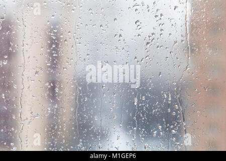 Im städtischen Hintergrund - Regen fällt auf Fensterglas (Fokus auf Wasser rieselt auf Fensterglas) im Winter Tag Stockfoto