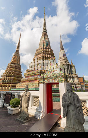 Zwei chinesische Statuen vor einem reich verzierten Tor und chedis des Wat Pho (Po) Tempelanlage in Bangkok, Thailand, an einem sonnigen Tag. Stockfoto