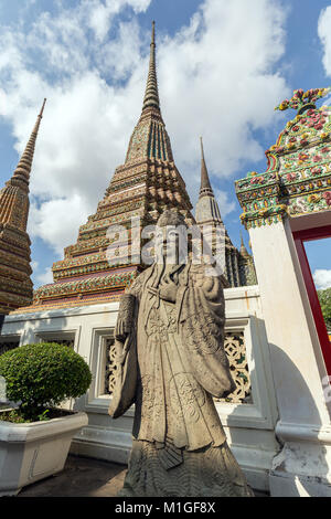 Nahaufnahme eines chinesischen Statue vor einem reich verzierten Tor und chedis des Wat Pho (Po) Tempelanlage in Bangkok, Thailand, an einem sonnigen Tag. Stockfoto
