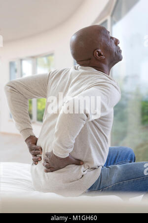 Afrikanische amerikanische Mann mit schweren Rückenschmerzen sitzen auf dem Bett in der Wohnung seines luxuriöse Schlafzimmer Stockfoto