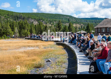 Touristen sitzen auf Bänken warten auf Old Faithful Geysir. Yellowstone National Park, Wyoming, USA Stockfoto
