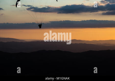 Schöne aufnahme eines Gleitschirms silhouette Fliegen über Monte Cucco (Umbrien, Italien) mit Sonnenuntergang im Hintergrund, mit schönen Farben und dunklen Töne Stockfoto