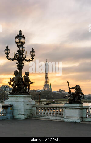 Blick auf den Eiffelturm von Pont Alexandre III bei Sonnenuntergang mit einer seiner Jugendstil Lampe, mit Putten verziert, im Vordergrund. Stockfoto