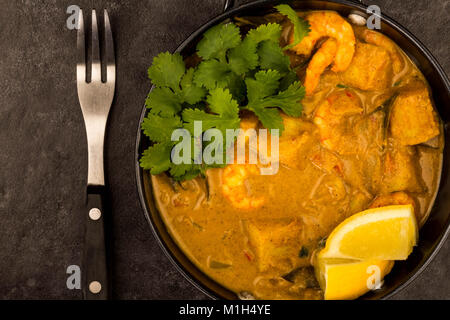 Sri Lanka Style King Prawn Curry mit Zitrone und Koriander Kräuter gegen einen schwarzen Fliesen Hintergrund Stockfoto