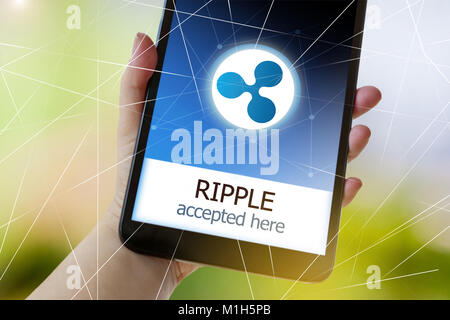 Virtuelles Geld cryptocurrency auf dem Bildschirm des Smartphones in einer Hand - Welligkeit (XRP) Hier akzeptiert Stockfoto