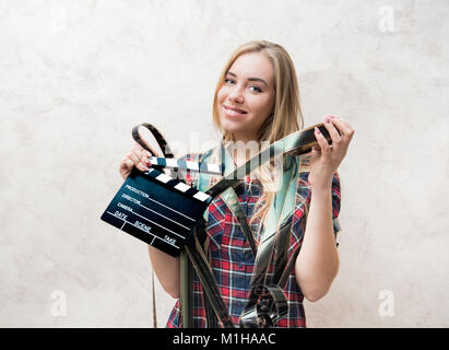 Schöne junge blonde Frau Student lächelte Kamera mit Klappe und 35 mm abgerollt Filmstreifen suchen Stockfoto