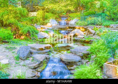 Einen schönen Wasserfall/Teich geworfen in das Licht der untergehenden Sonne. Grüne Pflanzen und Bäume umgeben das Wasser. Stockfoto