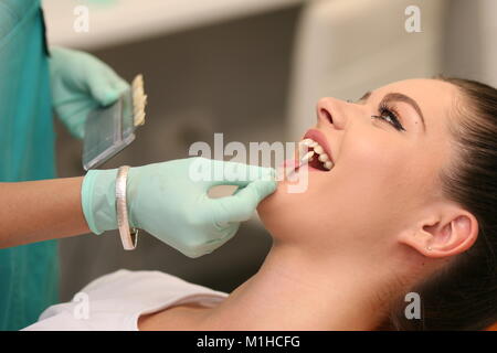 Eine junge hübsche Frau in einem Zahnarztstuhl sitzen, der Zahnarzt ist die Auswahl der Farbton der Zähne Farbe zu holen... Stockfoto