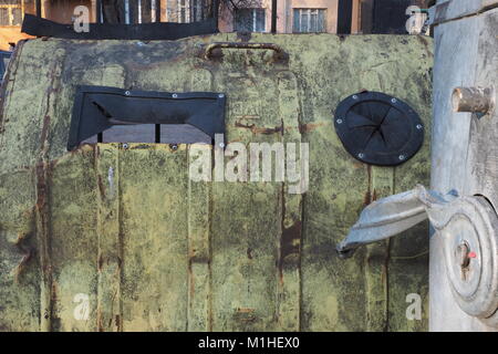 Metal grunge Hintergrund mit grünlichen Farbe mit schwarzer Gummieinlage, Vordergrund ein graues Metall curl, hinter einem rosa Haus mit Windows. Stockfoto