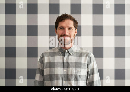 Lächelnden jungen Mann mit einem kariertem Hemd seine Tapete matching Stockfoto