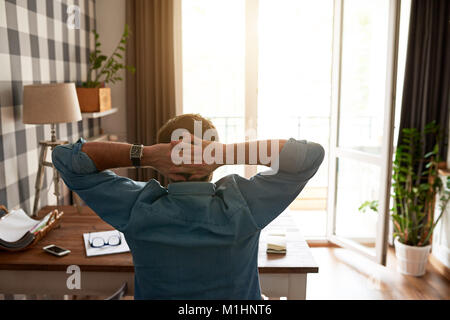 Mann lehnte sich in seinem Stuhl zurück, während die von zu Hause aus arbeiten Stockfoto