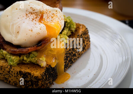 Avocado auf Toast mit pochiertem Ei und Speck Stockfoto