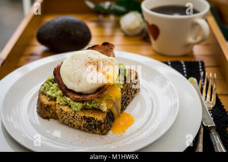 Zertrümmerte Avocado mit Speck und einem pochierten Ei Stockfoto