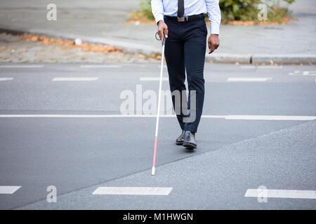 Blinde Person mit weißem Stick gehen auf die Straße Stockfoto