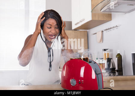 Frustriert Afrikanische junge Frau bei Burnt Toast aus der Toaster in der Küche Stockfoto