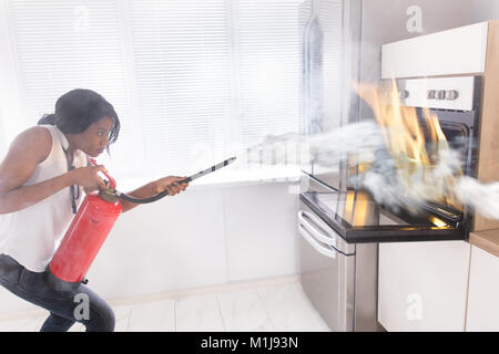 Junge afrikanische Frau mit Feuerlöscher zu stoppen, Feuer aus dem Ofen in der Küche Stockfoto