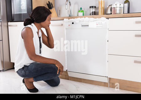 Traurig afrikanische Frau auf der Suche nach Schaumstoff aus der Spülmaschine in der Küche Stockfoto