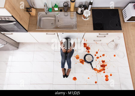 Enttäuscht afrikanische Frau sitzt auf der Küche Etage mit verschüttetem Essen in der Küche Stockfoto