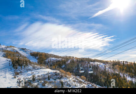 Winter Blick auf einem Berghang mit einer Gondel, die Steigung ist mit Bäumen und Schnee bedeckt; blauer Himmel mit Wolken über Stockfoto