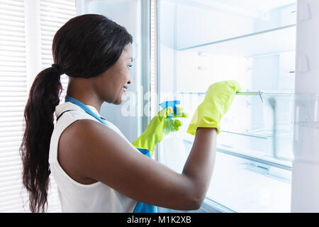 Junge afrikanische Frau tragen gelbe Handschuhe Reinigung öffnen Kühlschrank Stockfoto