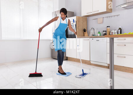 Hausfrau zu tun Multitasking Hausarbeit durch das Fegen und Wischen in der Küche Stockfoto