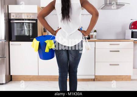 Rückansicht einer Frau mit Schaufel und Sprühflasche in der modernen Küche Stockfoto