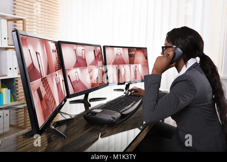 Junge afrikanische Business Geschäftsfrau Gespräch am Telefon während der Überwachung mehrerer Sicherheit Gesamtlänge im Büro Stockfoto