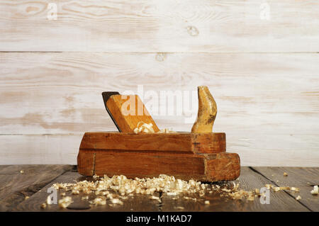 Alte Hobel- und Sägespäne auf dunklen Holztisch, weiße Wand Stockfoto