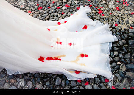 Schwanz von White's Braut Kleid mit roten Rosenblättern und Reis auf die Kirche stein Pflaster Stockfoto