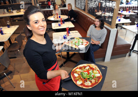 Kellnerin trägt Pizza in der Tabelle in eine Pizzeria in England Stockfoto